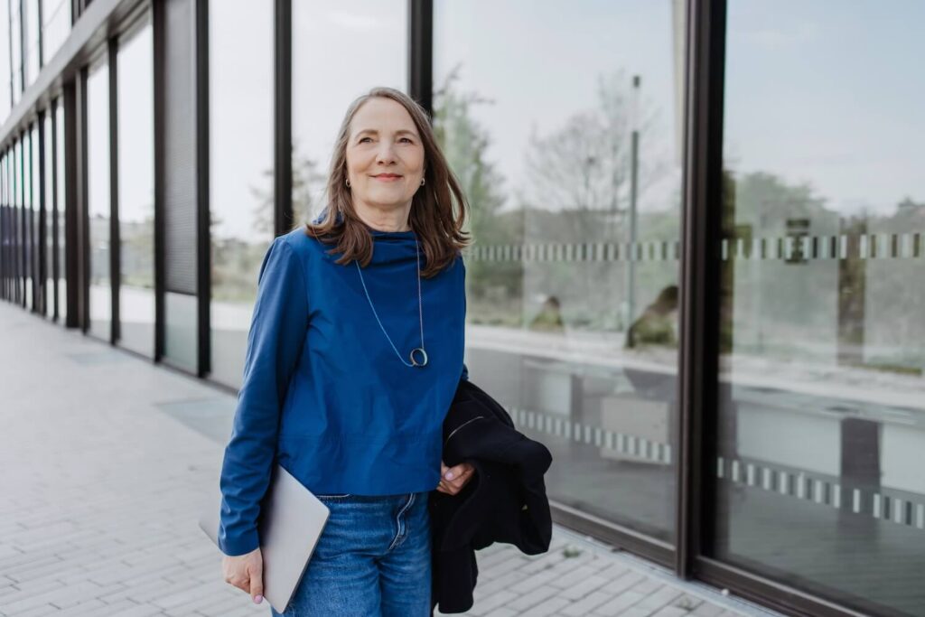Kerstin Reisinger läuft vor einem Glasgebäude mit einem Laptop unter dem Arm