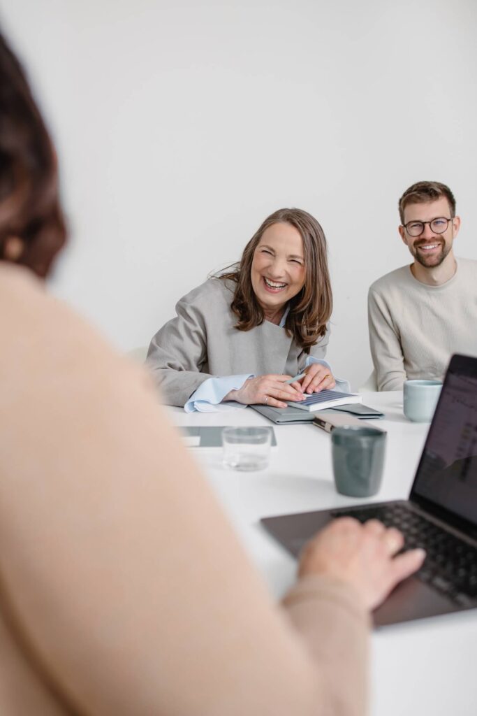Drei Mitarbeiter von GIB21 sitzen gemeinsam an einem Meetingtisch und lachen