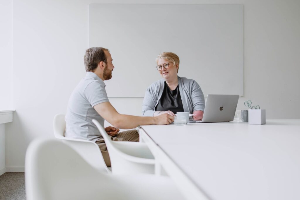 Ein Mann und eine Frau unterhalten sich in einem Meetingraum mit einem Laptop auf dem Tisch