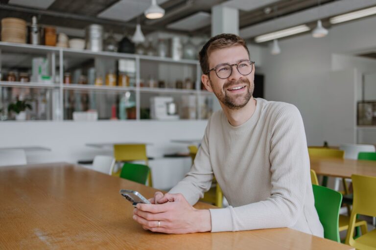 Lächelnder Mitarbeiter mit Smartphone in einer modernen Bürokantine
