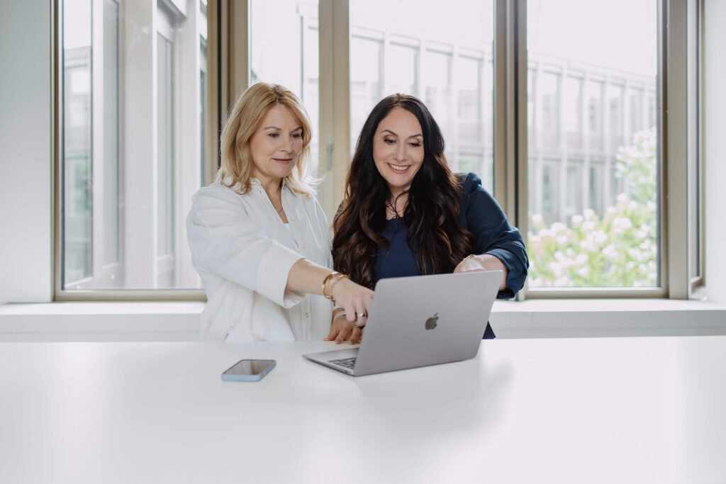 Zwei Frauen unterhalten sich während sie auf ein Macbook schauen