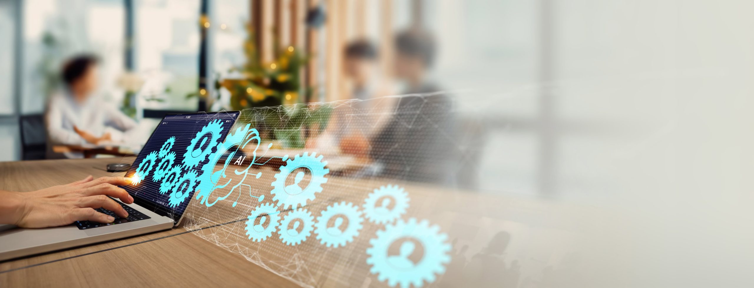 Hände tippen auf Laptop, darüber vernetzte Zahnräder und ein zentrales AI-Symbol vor unscharfem Konferenztisch